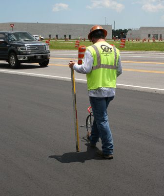 ATS QC Roadway Tech using measuring wheel on new pavement while holding a level straightedge